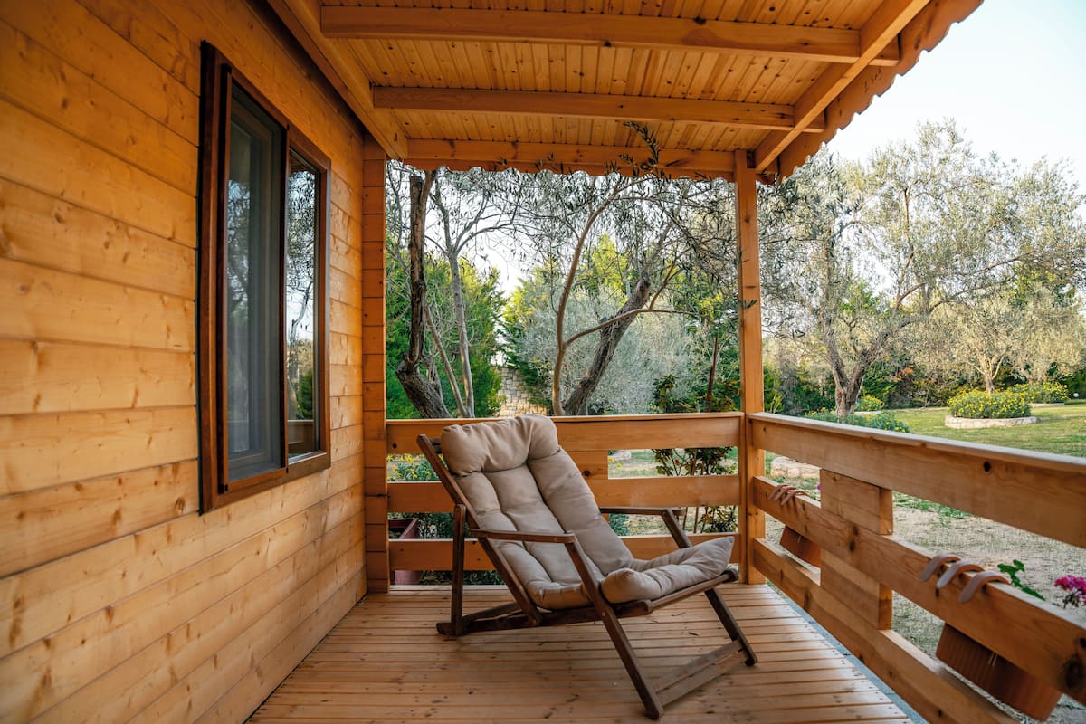 Una terraza de madera con una silla acolchada y un banco de madera.