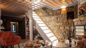 Ein gemütliches Wohnzimmer mit Steinwand, Kamin, Bücherregal und einem roten Sessel.