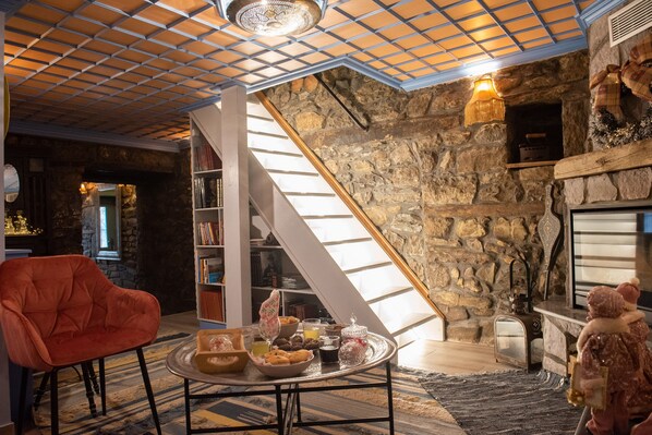 A cozy living room with a stone wall, a fireplace, a bookshelf, and a red armchair.