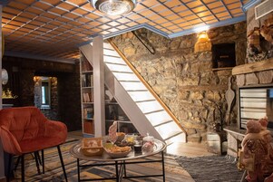 Una sala de estar acogedora con una pared de piedra, una chimenea, una estantería y un sillón rojo.