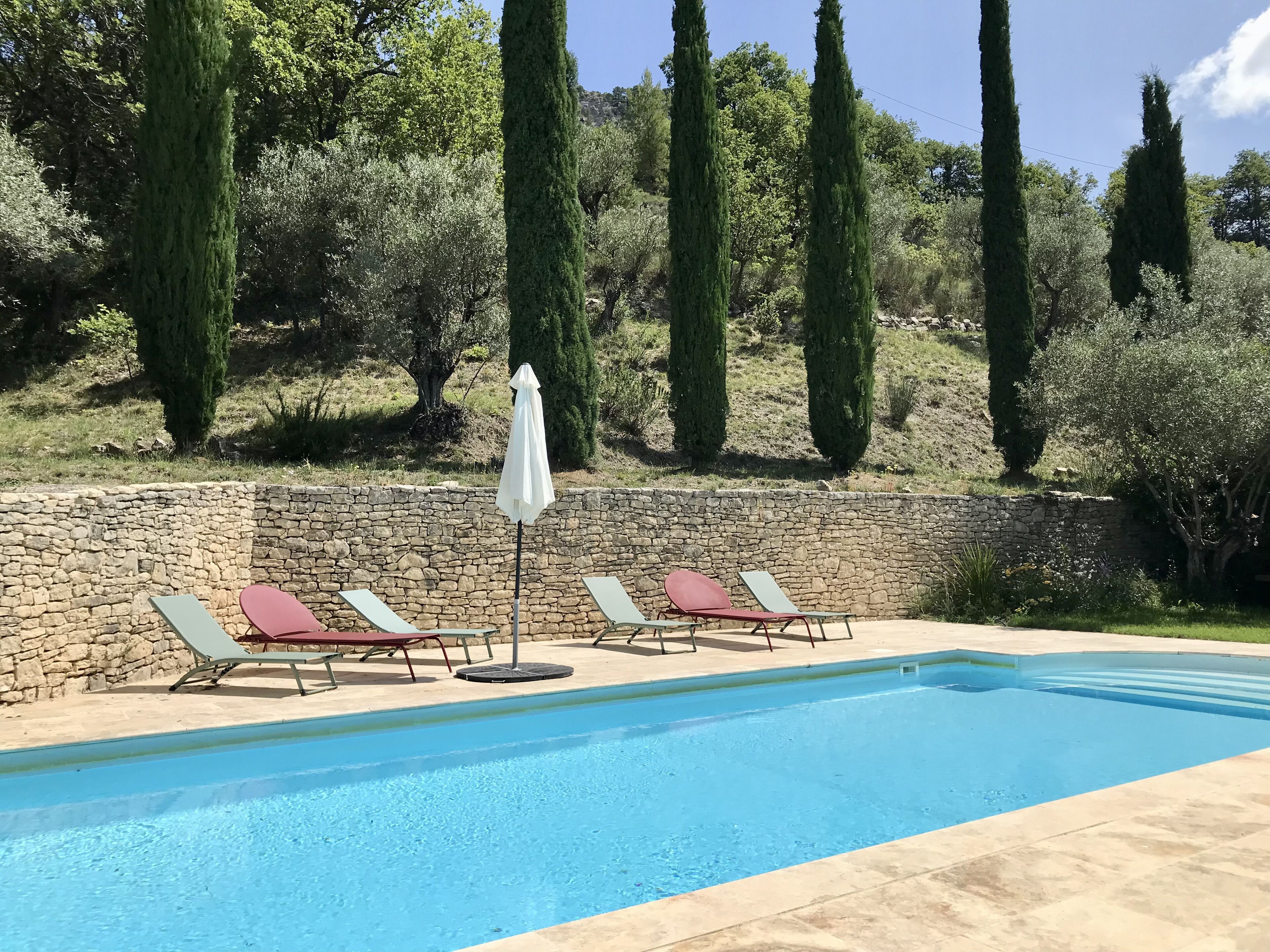 A pool with stone walls and lounge chairs.