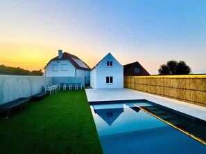 Een modern huis met een zwembad, een gazon en een houten omheining.