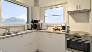 A modern kitchen with stainless steel appliances, white cabinetry, and a view of a lake. - Vacation home Staedenbergh in rural Staden! 10 pers (Staden)