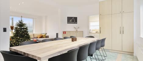 Un comedor moderno con una mesa de madera, sillas negras, un árbol de Navidad y una cocina al fondo.