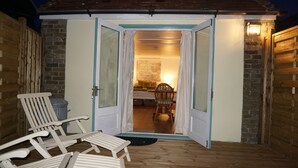En liten, öppen struktur med ett trädäck, två vita loungestolar och en mur av tegelsten.