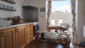 Ett kök med träskåp, en diskho och en matplats med ett bord och stolar. Det finns ett fönster med gardiner och en skylt med texten "STRAND".