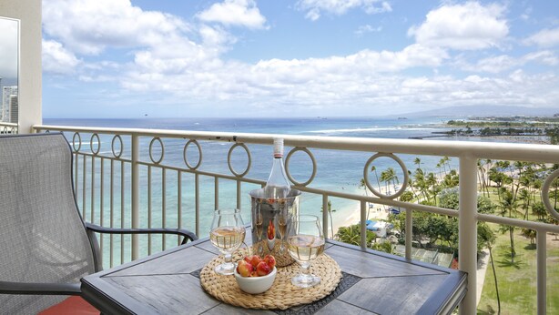 Un balcon avec une table dressée pour deux personnes, donnant sur une plage et l’océan.
