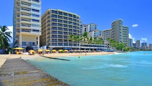 Un hôtel situé en bord de mer, avec plusieurs étages, des parasols sur la plage et une plage de sable.