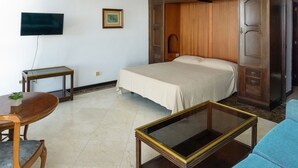Una stanza con un letto, una televisione a parete, un armadio in legno, un tavolino con una pianta e un divano blu.