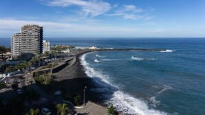 Panoramica costiera con una passeggiata lungomare, un hotel alto e un molo roccioso.