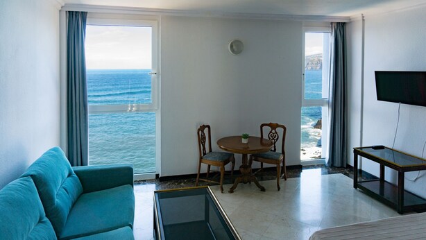 Una stanza con vista sull'oceano, un divano, un tavolino e una TV.