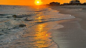 A beach with a sunset, waves, and houses in the background. - Ocean Dreams Beachfront Home Stunning Views Like New Sleeps 10 4 BR 3 Full Baths (Gulf Shores)