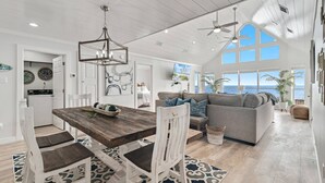 A spacious living area with a large wooden dining table, white chairs, a gray sofa, and a ceiling fan. - Ocean Dreams Beachfront Home Stunning Views Like New Sleeps 10 4 BR 3 Full Baths (Gulf Shores)