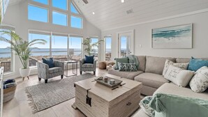 A spacious living room with a high ceiling, large windows, and a view of the ocean. There are two armchairs, a sofa, and a coffee table. - Ocean Dreams Beachfront Home Stunning Views Like New Sleeps 10 4 BR 3 Full Baths (Gulf Shores)