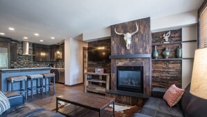 A modern living room with a stone fireplace, leather sofa, and a bar area with stools. - Zephyr Mountain Lodge, Condo | 3 bedroom Ski Slope Views (Premium rated Condo 2407) (Winter Park)