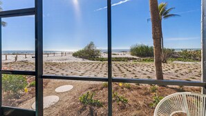 Blick durch ein Fenster auf einen Strand und Palmen im Hintergrund.