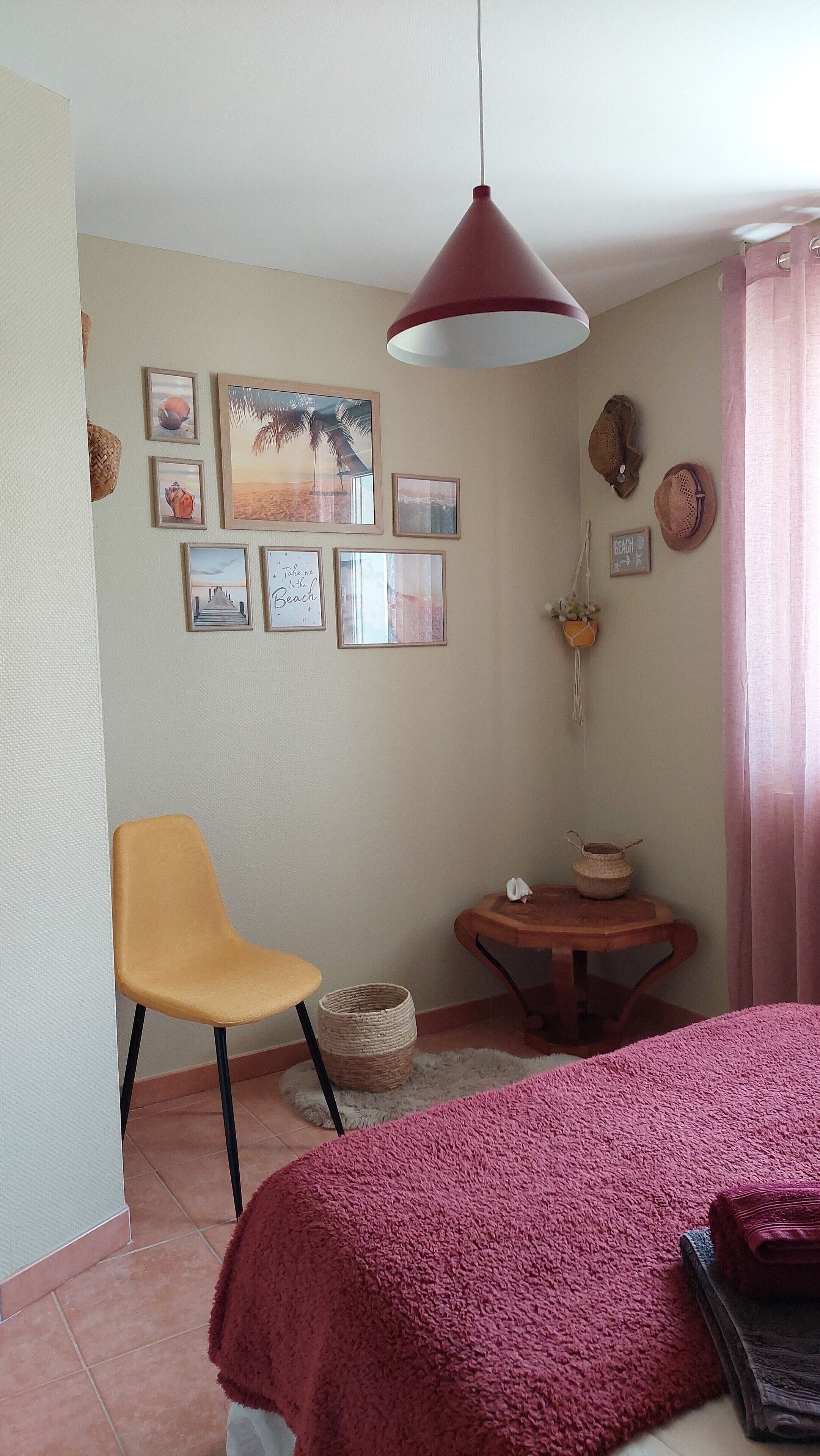 Ein Zimmer mit einem Bett, einem Sessel, einem Tisch mit einem Korb und Wanddekorationen, darunter gerahmte Bilder und ein Schild.