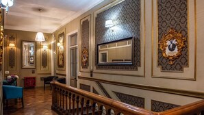 Un amplio pasillo con decoraciones ornamentales en las paredes, una escalera de madera y un sillón azul.