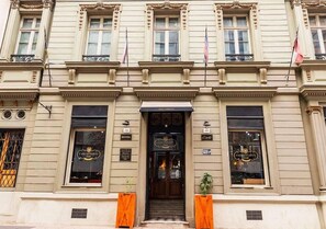 Un edificio histórico con una entrada central, ventanas amplias a ambos lados y un cartel que indica que es un hotel.