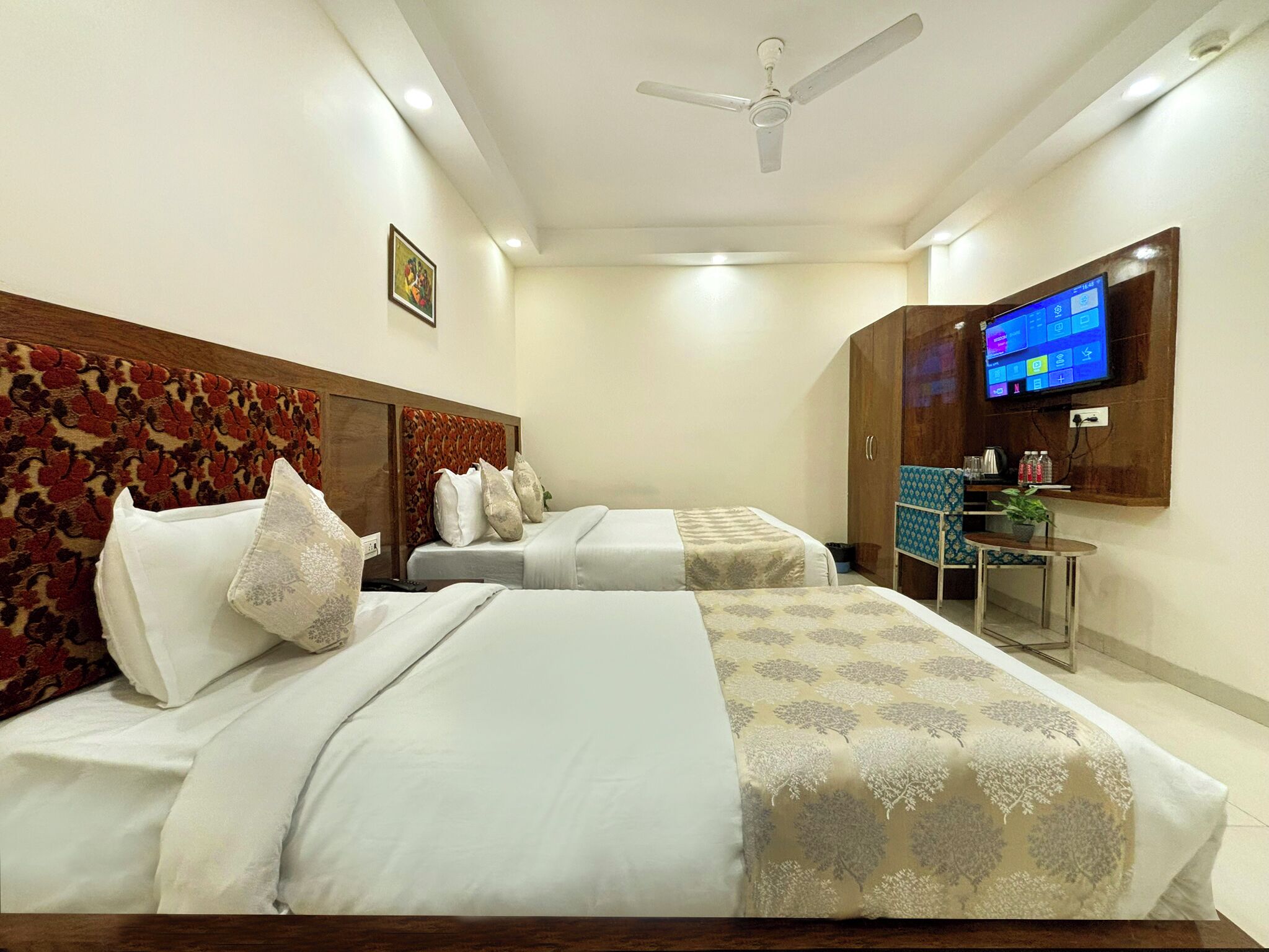 A hotel room with two beds, a TV, a desk, and a ceiling fan.