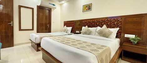 A hotel room with two beds, a wooden headboard, a mirror, an air conditioning unit, and a small plant on the nightstand.
