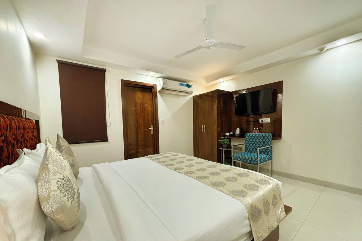 Una habitación de hotel con cama, escritorio, silla, televisor y aire acondicionado.