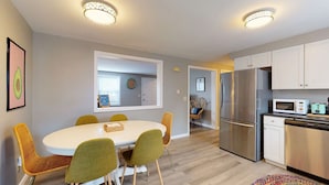 A modern kitchen with a stainless steel refrigerator, microwave, and dishwasher. There is a dining area with a round table and green chairs. - 5 Min Walk to Beach and Pier (Old Orchard Beach)