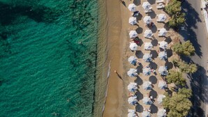 An aerial view of a beach with clear turquoise water, a sandy shore, and numerous white umbrellas providing shade. - Naxian Soul (Naxos)
