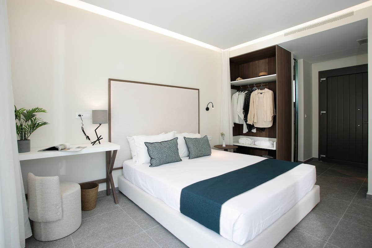 A modern hotel room with a large bed, bedside tables, a desk, and a wardrobe.