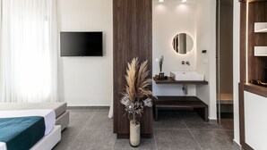 A modern hotel room with a bed, a flat-screen TV, a wooden column, a bathroom with a sink and mirror, and a vase with dried plants. - Naxian Soul (Naxos)
