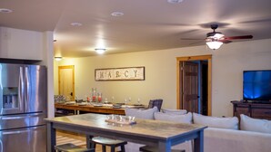 A modern kitchen with a built-in refrigerator, a dining area with a bar stool, and a living room with a television. - Beautiful 6-bed, 4.5-bath with private outdoor space.  5min walk to Main Street. (Lake Placid)