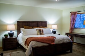 A neatly made bed with a wooden headboard, two bedside tables with lamps, a small plant, and a desk with a chair. - Beautiful 6-bed, 4.5-bath with private outdoor space. 5min walk to Main Street. (Lake Placid)