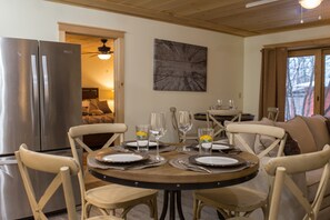 A dining area with a round table set for four, surrounded by four chairs. A large window with curtains is visible in the background. - Beautiful 6-bed, 4.5-bath with private outdoor space. 5min walk to Main Street. (Lake Placid)