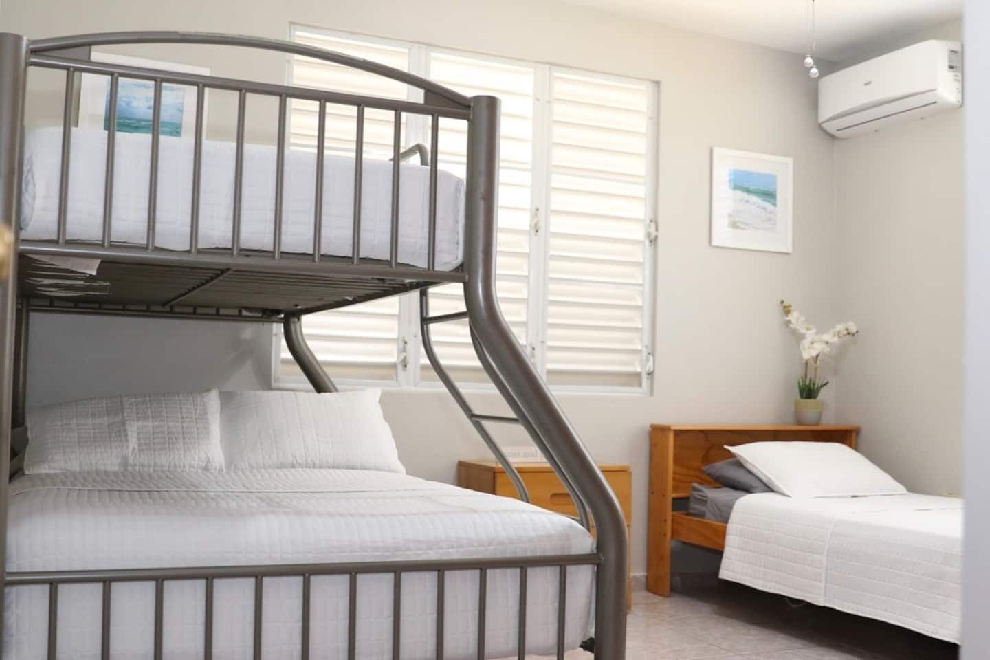 A bunk bed with white bedding, a wooden nightstand, a small bedside table, and a potted orchid.
