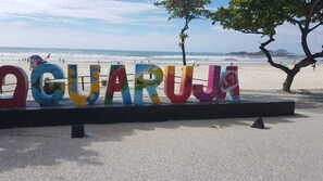 Cena de praia com letras coloridas formando a palavra 'OGUARUJA' sobre uma plataforma preta.