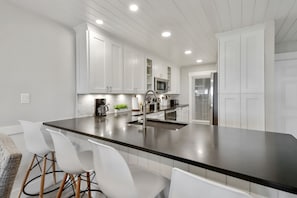 A modern kitchen with white cabinetry, a large black countertop, and stainless steel appliances.