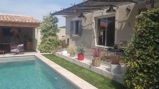A swimming pool with a patio area, surrounded by potted plants and a hanging chair.