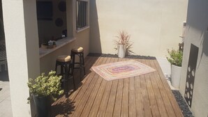 A wooden deck with a bar area, two stools, a colorful rug, and potted plants.