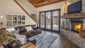 Una sala de estar acogedora con chimenea de piedra, sofás de cuero y un amplio ventanal con vistas a un paisaje nevado.