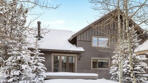 Una casa de madera de dos pisos con tejado cubierto de nieve y árboles circundantes.
