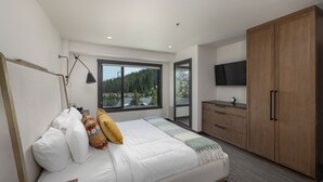 A modern bedroom with a large bed, a nightstand, a desk, a wardrobe, a TV, and a window with a view of trees. - Shoshone Ski-In/Out w/ amazing views, community hot tub/pool/fitness center & fireplace! (Big Sky)