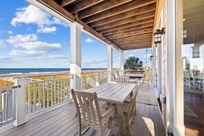 Een houten terras met een tafel en stoelen, met uitzicht op een strand en een heldere lucht.