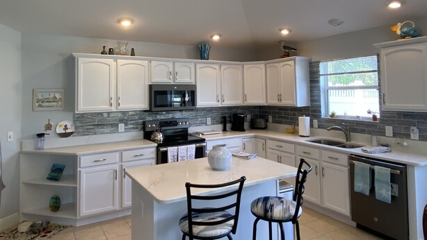 A modern kitchen with white cabinets, a central island, a microwave, and a dishwasher. - Beautifully Decorated Sm Dog Friendly Villa w/BBQ, BICYCLES & WiFi! (The Villages)