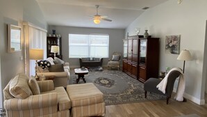 A living room with a sofa, ottoman, armchair, and a large wooden cabinet. - Beautifully Decorated Sm Dog Friendly Villa w/BBQ, BICYCLES & WiFi! (The Villages)