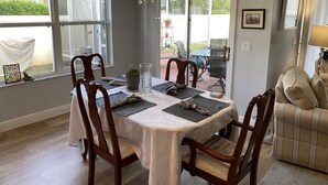 A dining area with a table set for four, surrounded by wooden chairs, a chandelier, and a view through a glass door to an outdoor patio. - Beautifully Decorated Sm Dog Friendly Villa w/BBQ, BICYCLES & WiFi! (The Villages)