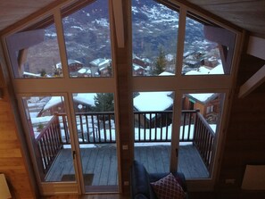 Une cabane en bois dotée d’une grande fenêtre donnant sur un paysage montagneux enneigé.