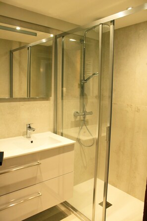A modern bathroom with a glass-enclosed shower, a white sink, and a large mirror above the vanity.