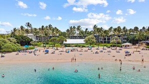 A beach with clear turquoise water, people swimming and sunbathing, and palm trees.