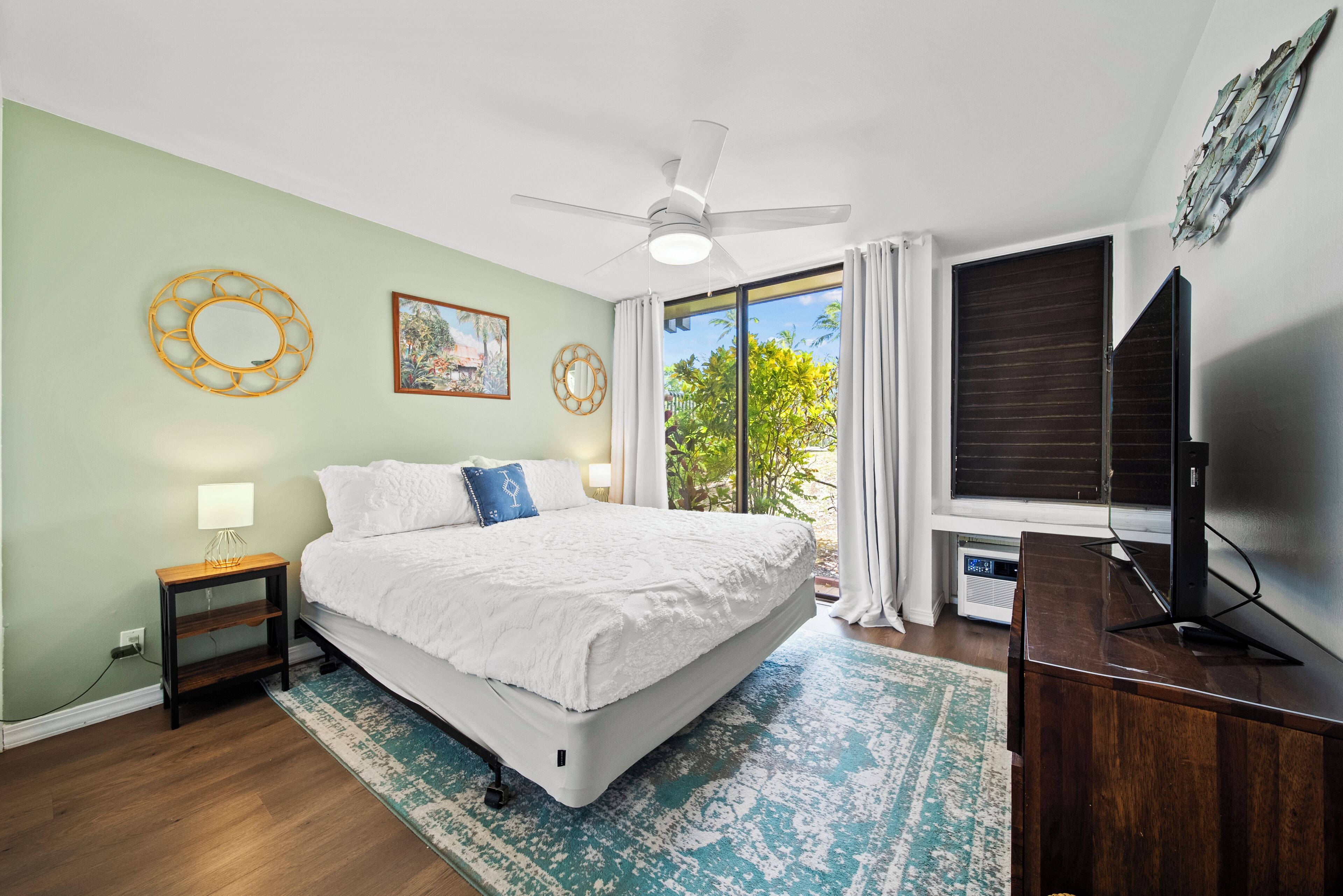 A bedroom with a bed, a ceiling fan, a TV, and a window with curtains.