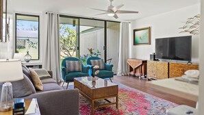 A modern living room with a sofa, armchair, coffee table, TV, and a ceiling fan.